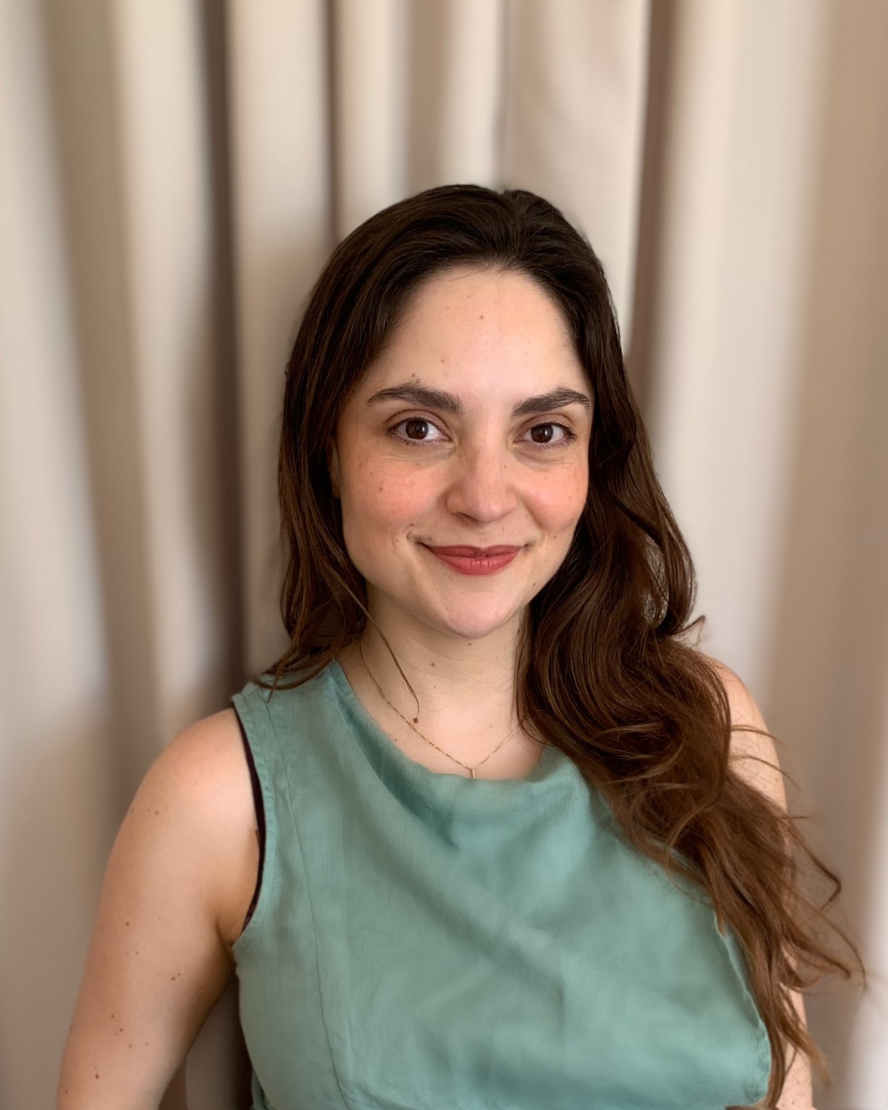Paola del Bosque smiling in front of a neutral curtain